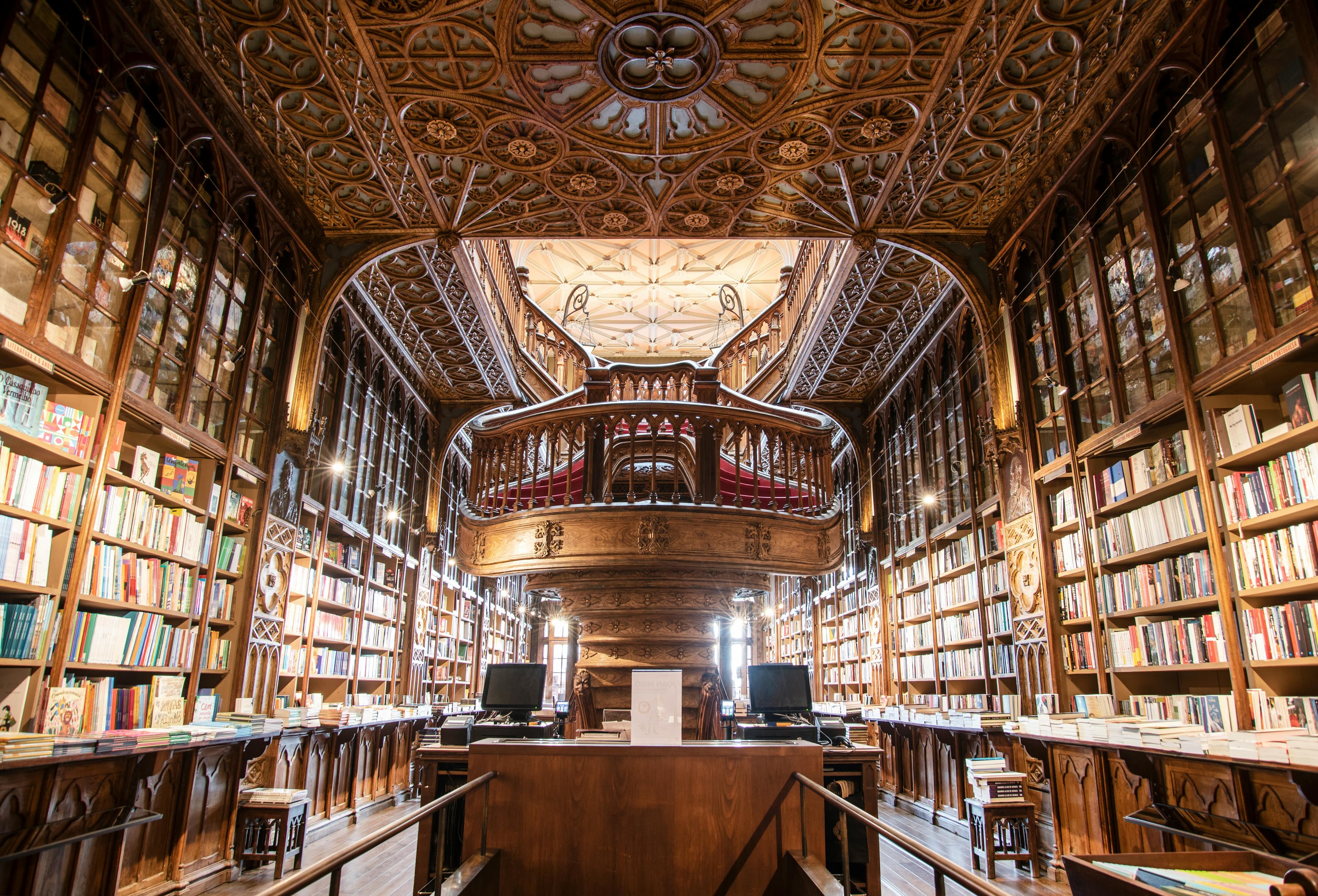 Opulent library interior featuring ornate woodwork, a grand balcony, and shelves filled with colorful books under an intricately designed ceiling.