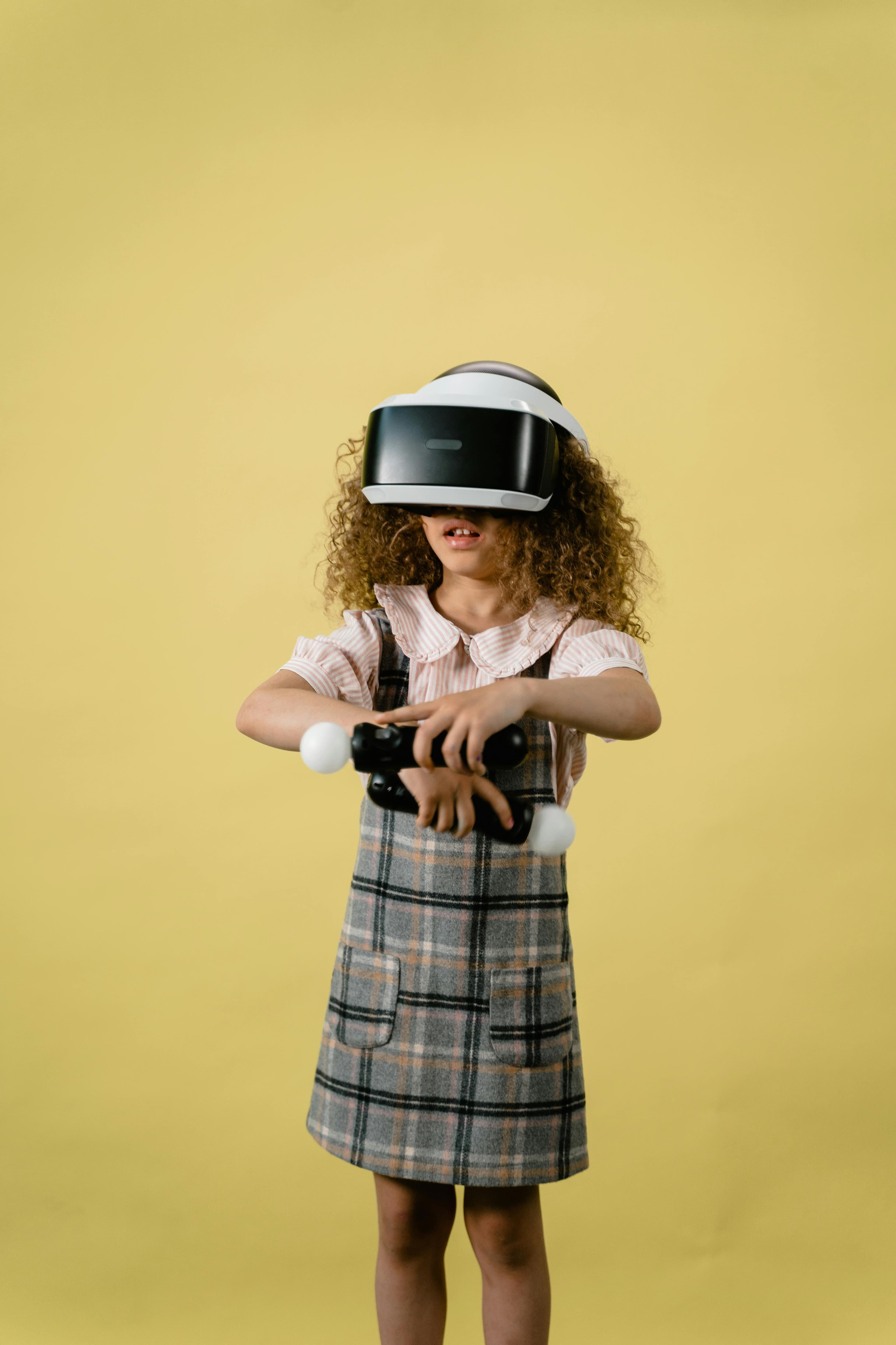 A child wearing a virtual reality headset is holding a gaming controller, standing against a vibrant yellow background.