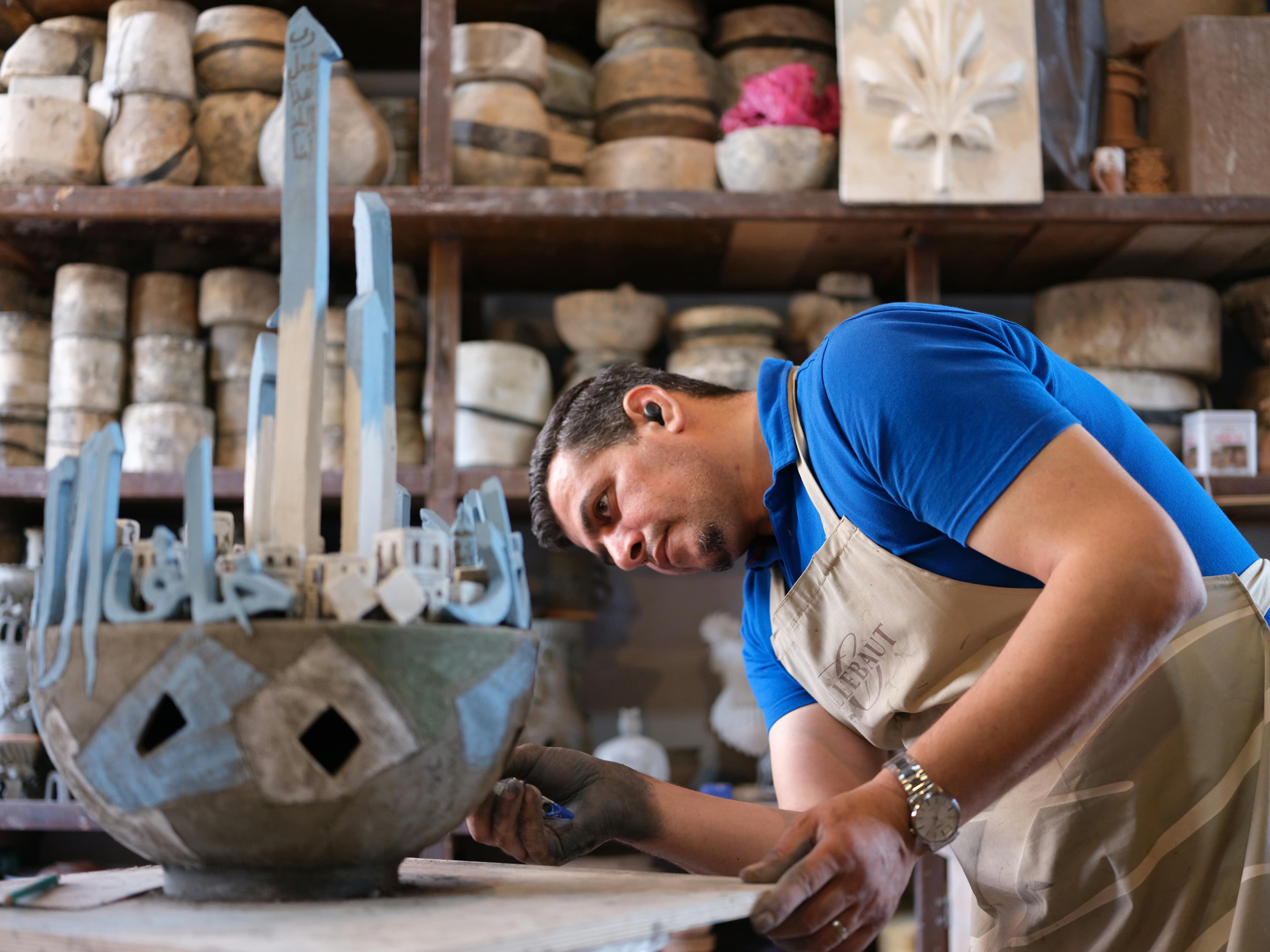 A skilled artisan focuses on a clay sculpture adorned with blue and white patterns, surrounded by various pottery pieces on shelves.